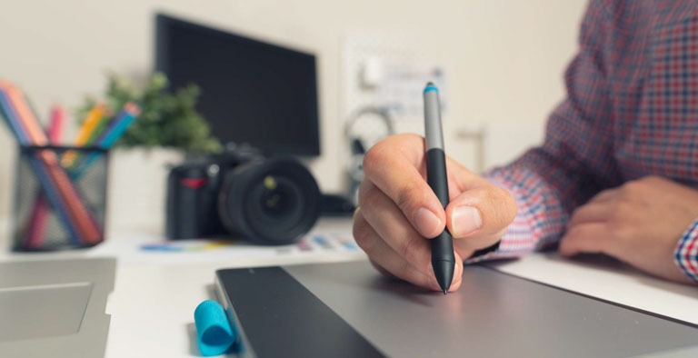 Photo ID: B05. Graphic designer working on digital tablet. Camera on desk in background. Photographer working at office.