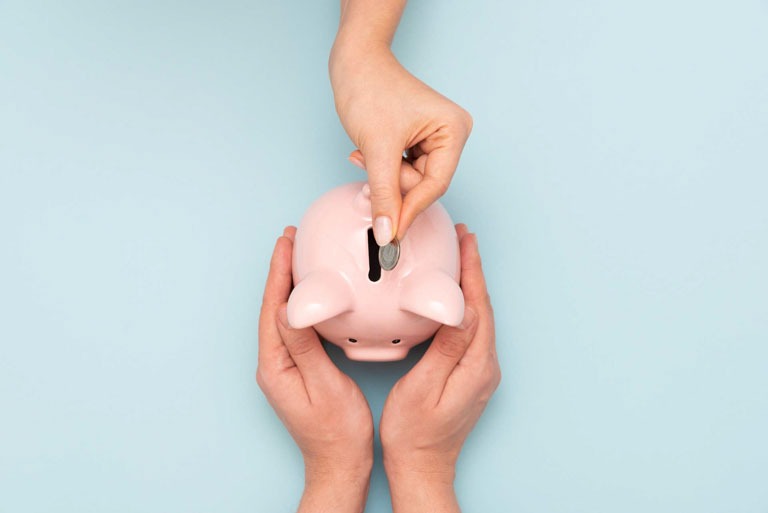 Photo ID: B20. Hand putting coin to piggy bank, top view. Pink piggy bank on blue background