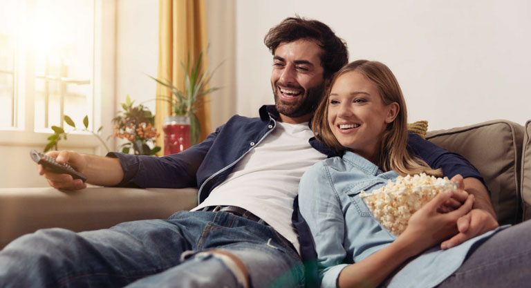 Photo ID: L04. Couple watching TV, eating popcorn on a sofa at home