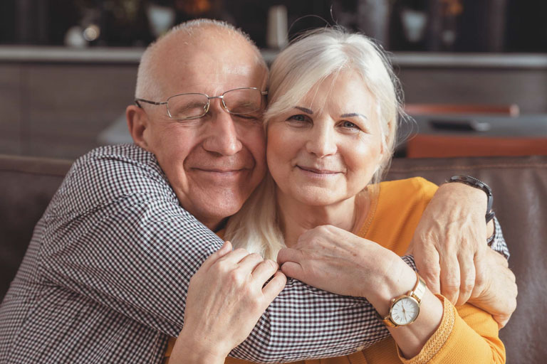 Photo ID: L13. Cheerful, romantic senior couple hugging while sitting on sofa at home