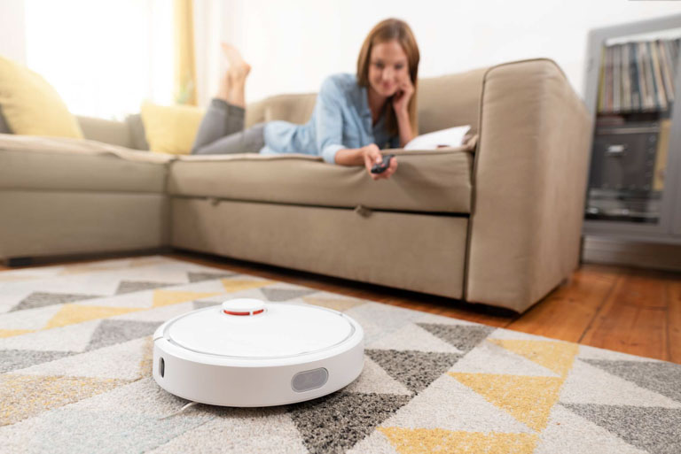 Photo ID: T04. Robotic vacuum cleaner cleaning the room while woman relaxing on sofa.